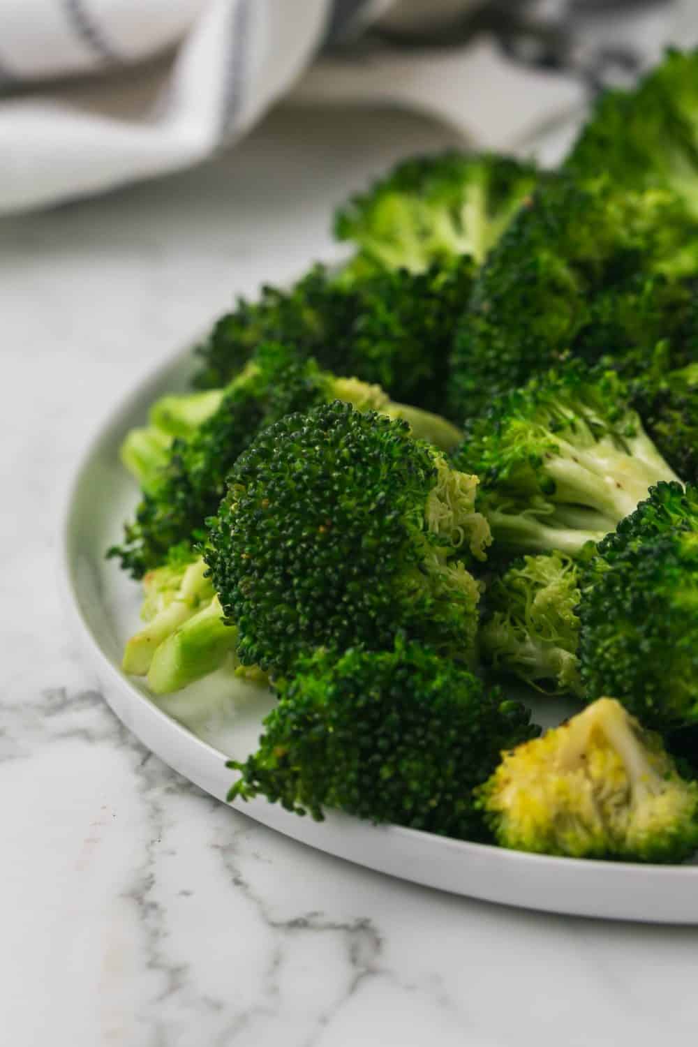 close up of view of a round white plate of sautéed broccoli