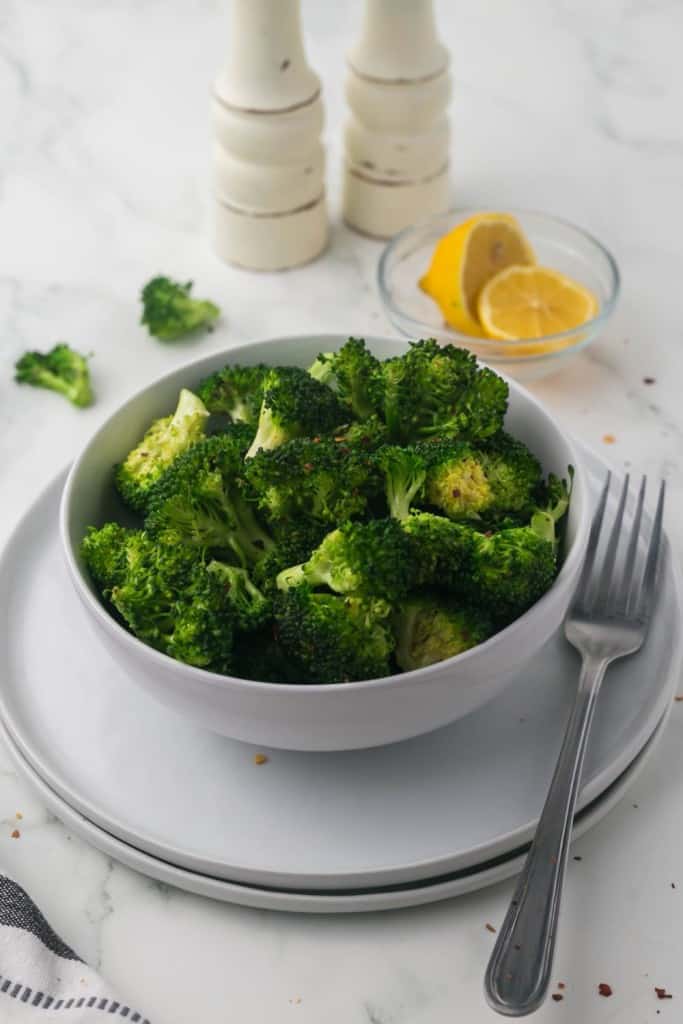 a bowl of sautéed broccoli and with lemon and salt and pepper grinders