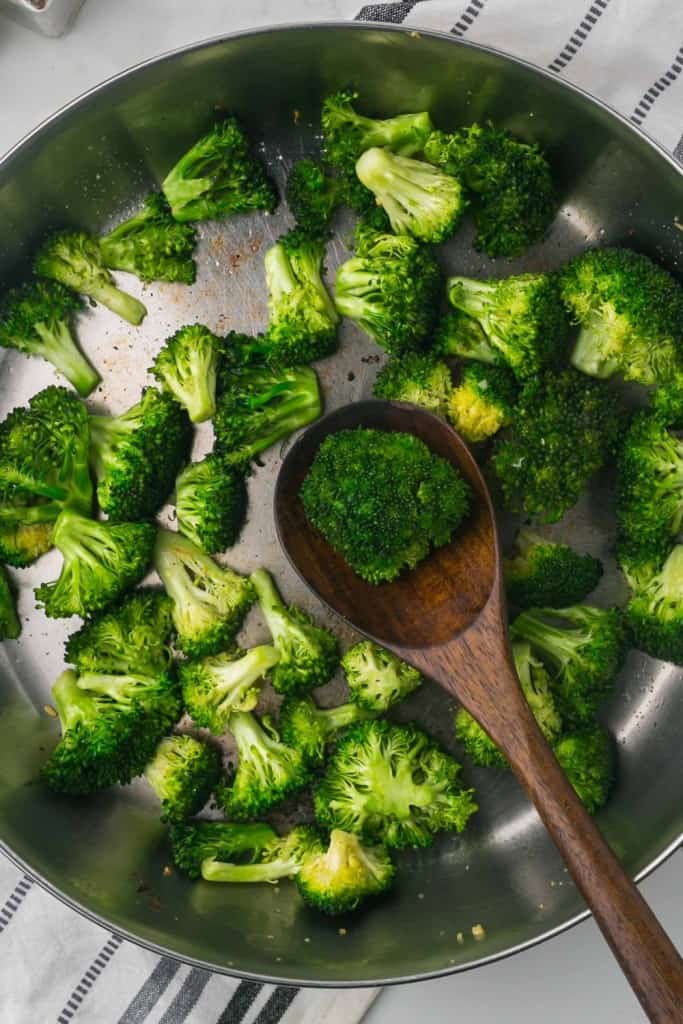 sautéed pan of broccoli and a wooden spoon top view close up