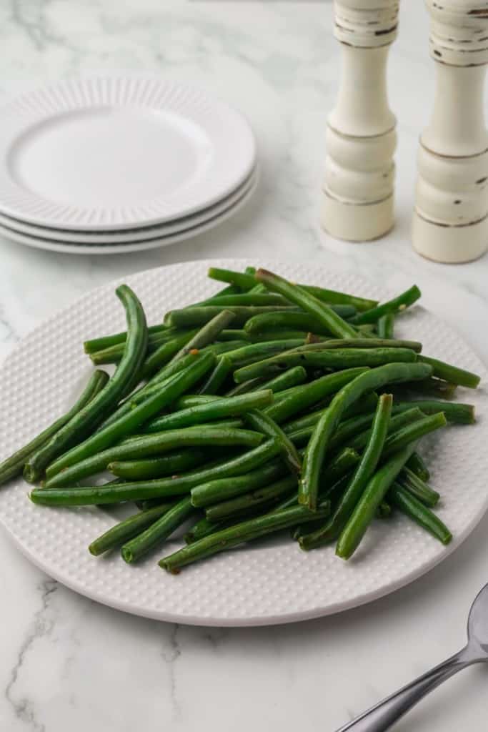 a white plate of sautéed green beans