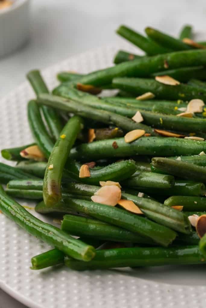 a white plate of sautéed green beans with almonds on top
