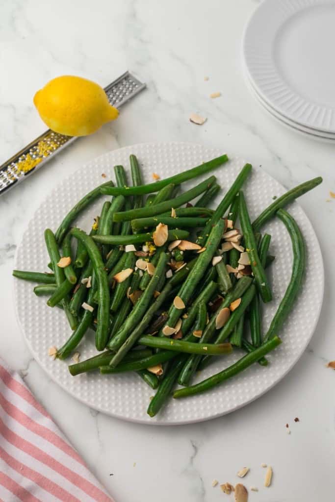 top view of a white plate of sautéed green beans with lemon zest and almonds