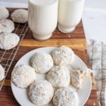 white round powdery Italian wedding cookies on white plate with a glass of milk