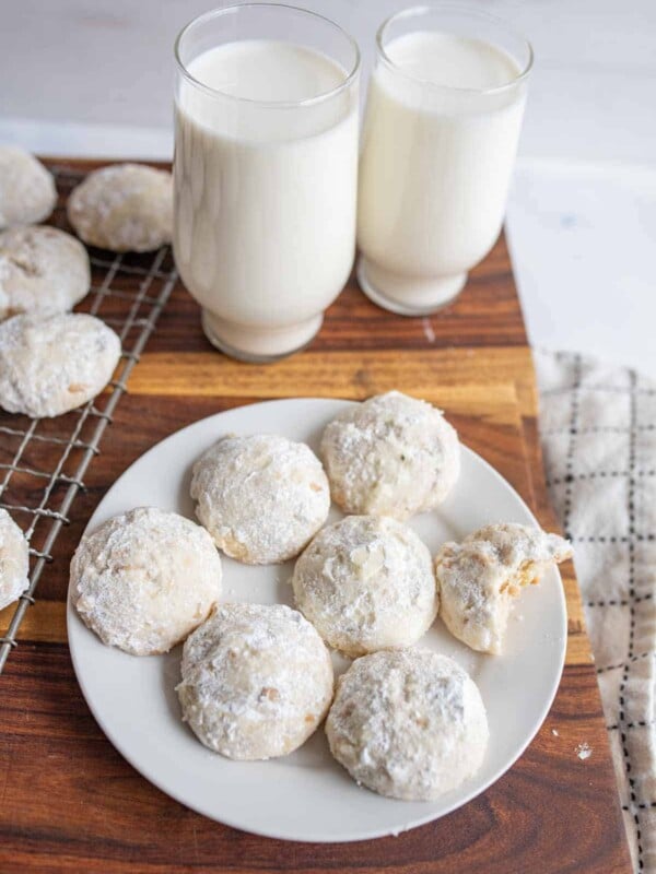 white round powdery Italian wedding cookies on white plate with a glass of milk