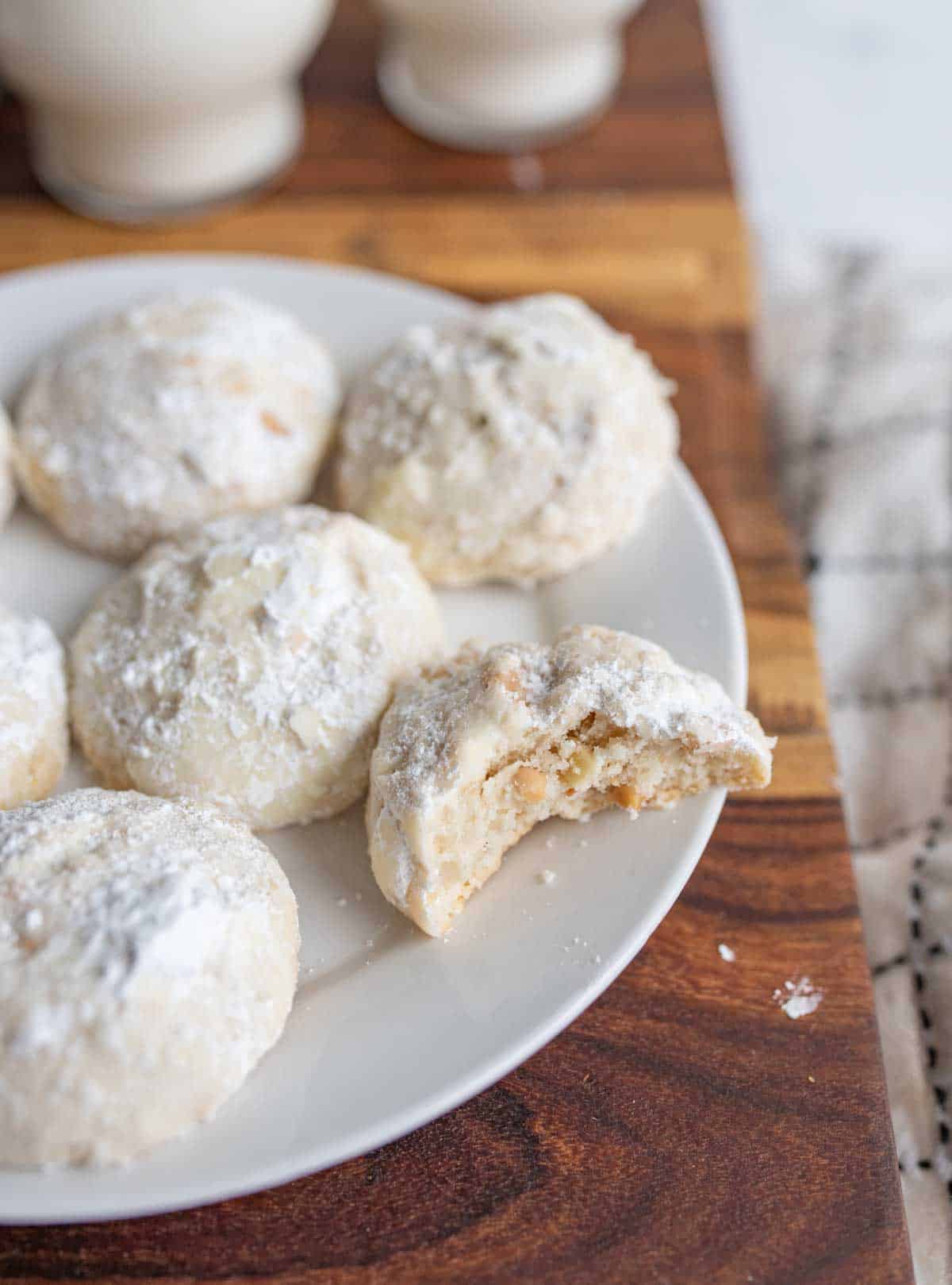 white round powdery Italian wedding cookies on white plate with a bite taken out