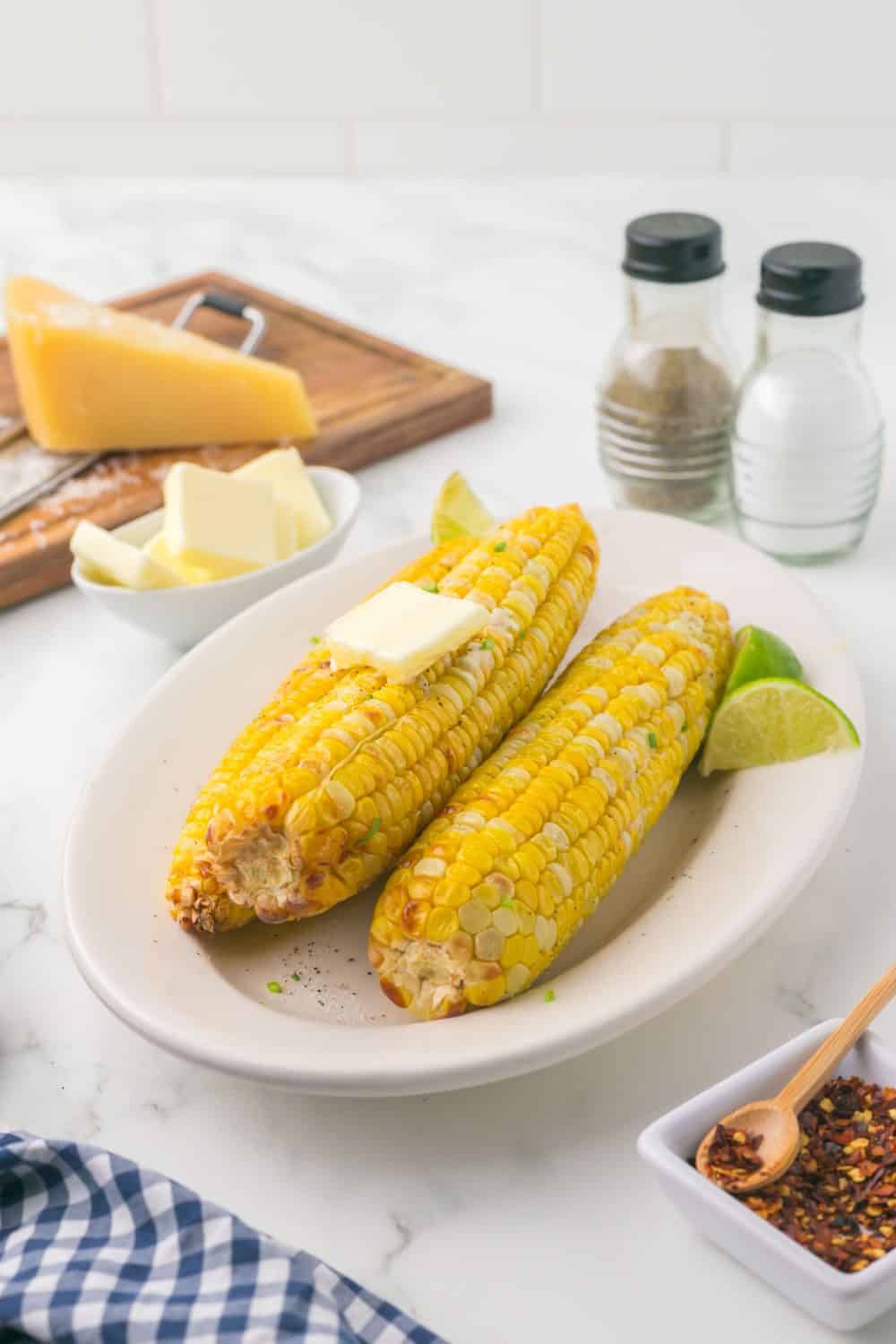 air fryer corn on the cob on a plate and seasonings and butter all around