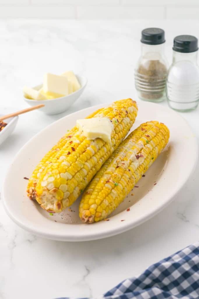 air fryer corn on the cob on a plate and seasonings and butter all around
