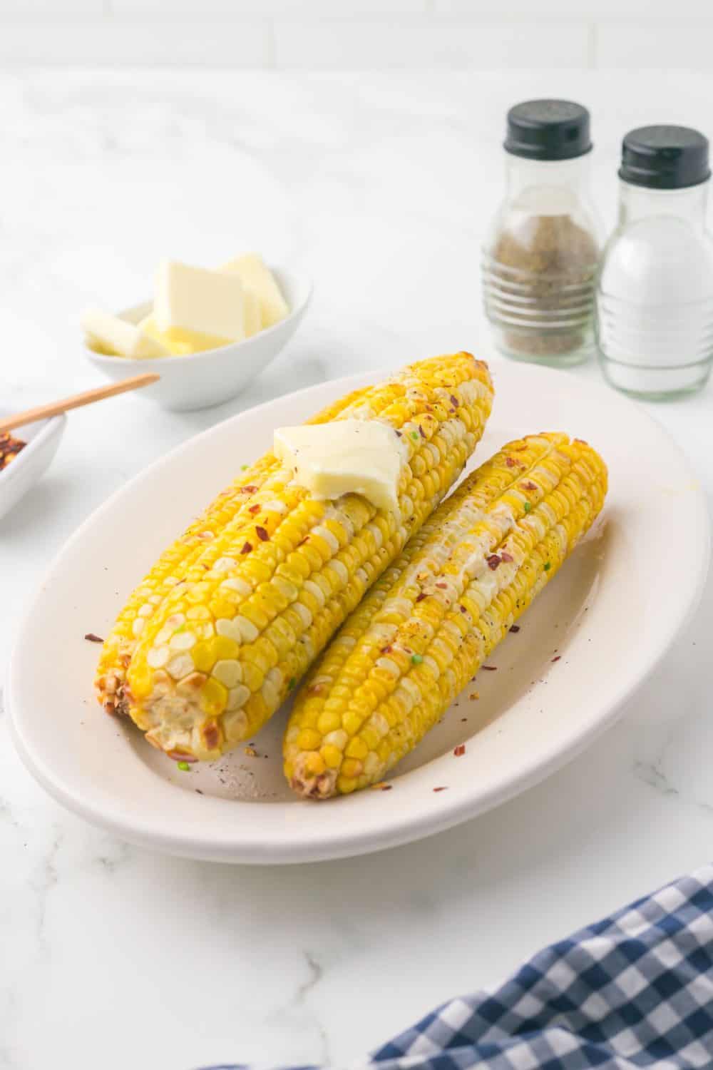 air fryer corn on the cob on a plate and seasonings and butter all around