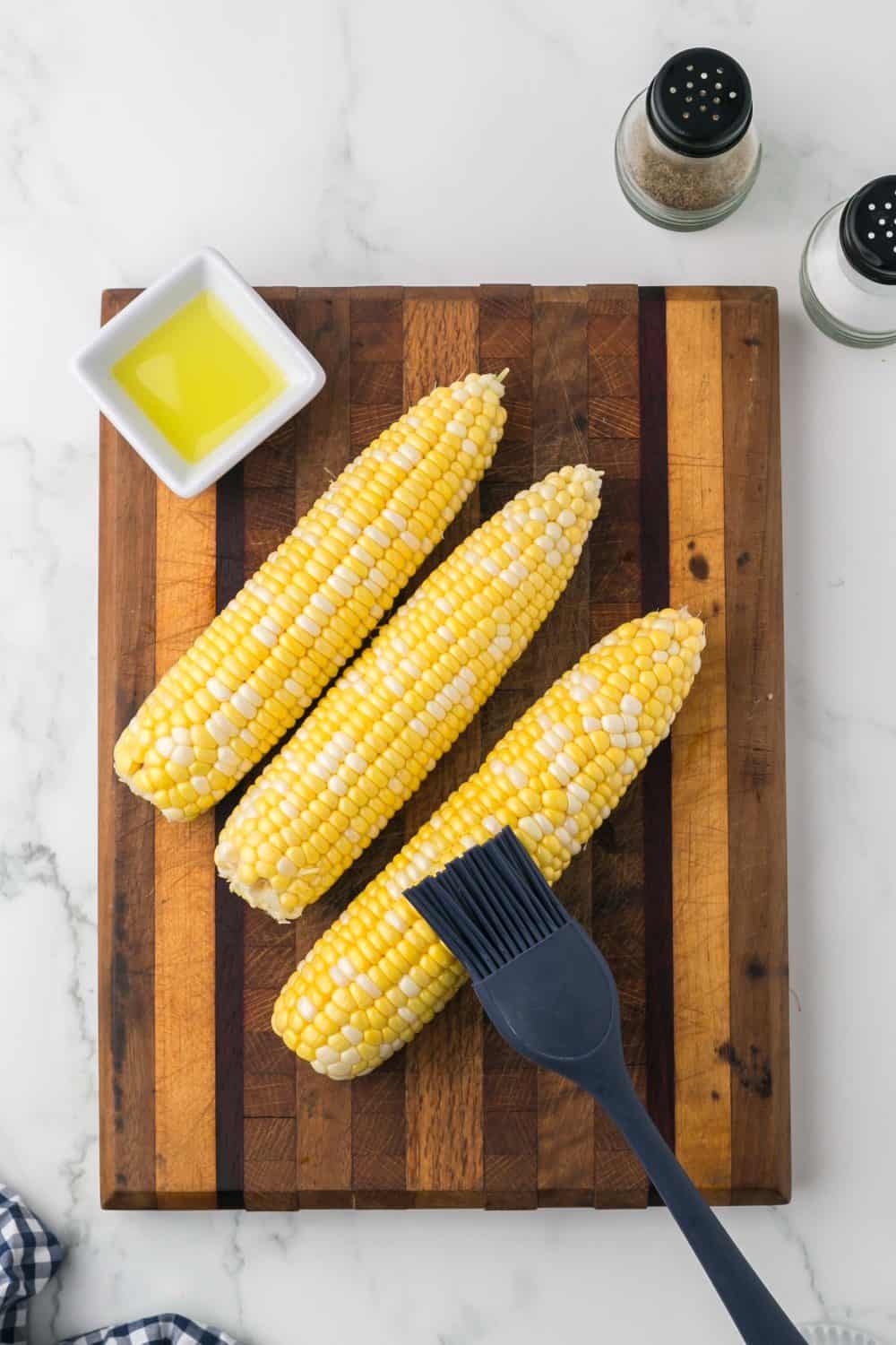 brushing butter on raw corn cobbs