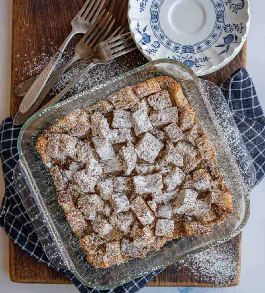 clear baking dish of squares of bread pudding with powdered sugar atop