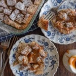 clear baking dish of squares of bread pudding with powdered sugar atop and served onto classic china dishes on the side with caramel on top