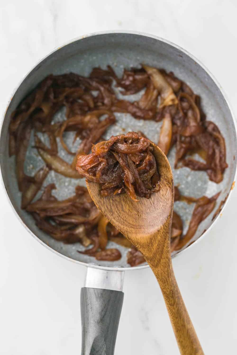 close up of finished caramelized onions on a wooden spoon