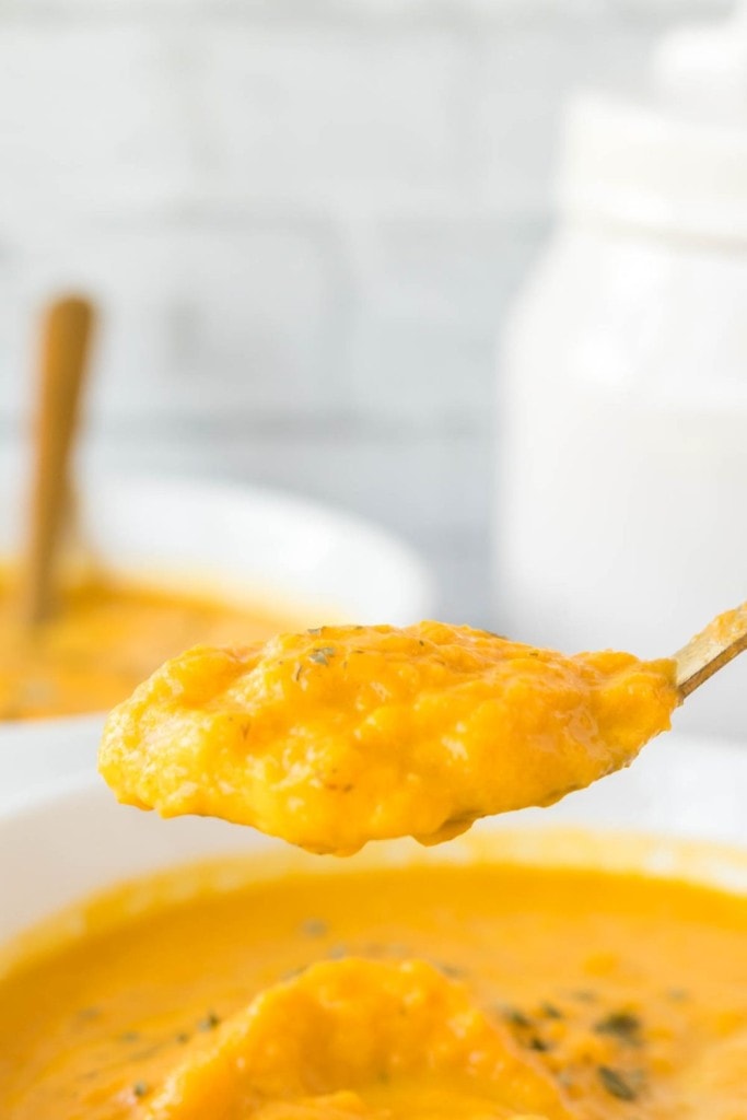 two bowls of bright orange carrot soup on a golden spoon