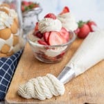 Chantilly cream piped out onto a cutting board with fruit in the background.