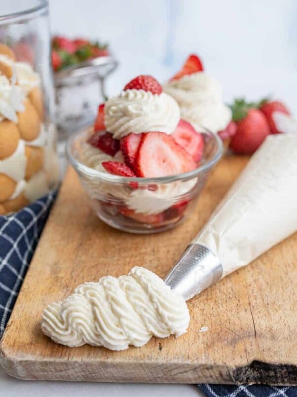 Chantilly cream piped out onto a cutting board with fruit in the background.