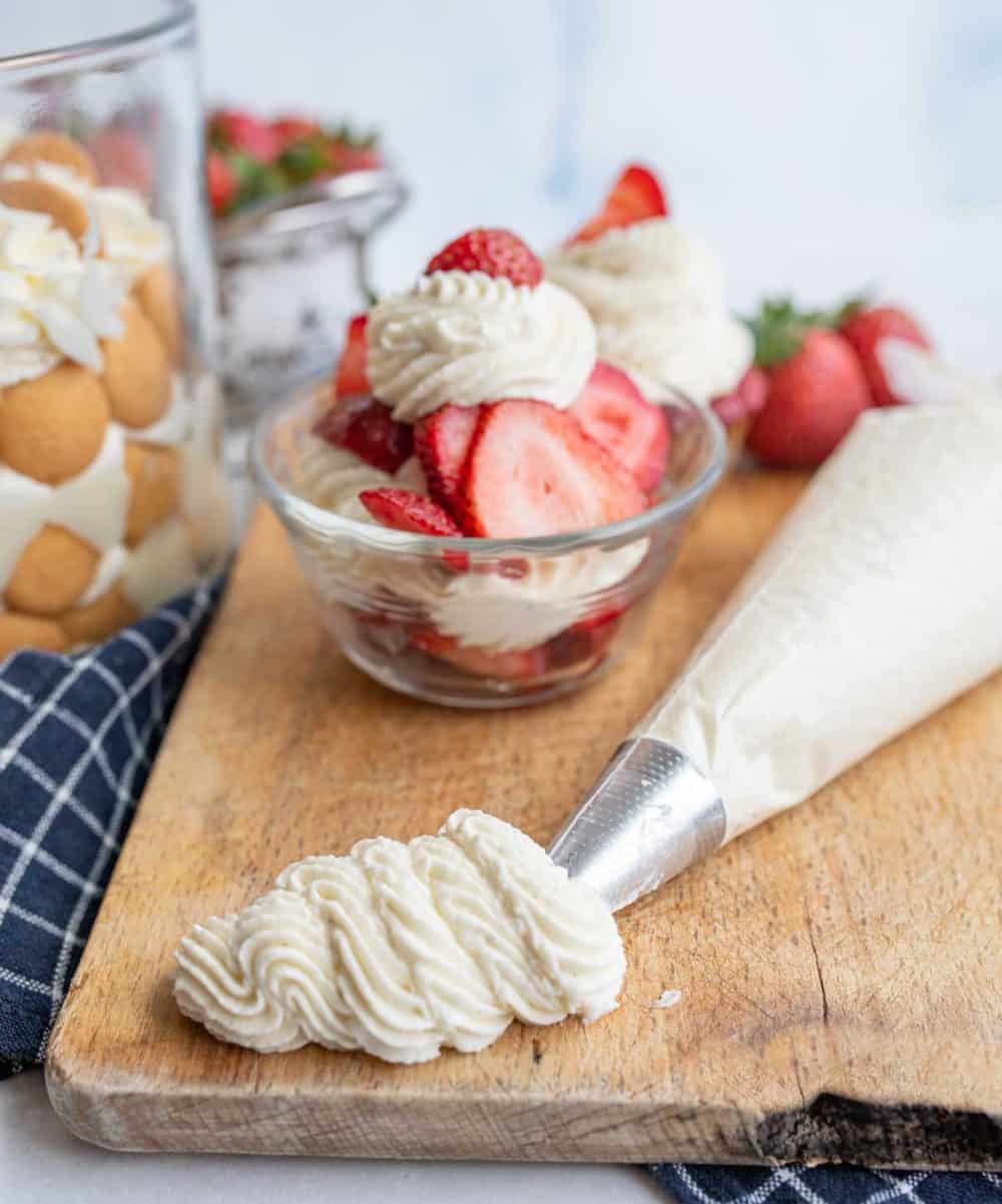 Chantilly cream piped out onto a cutting board with fruit in the background.