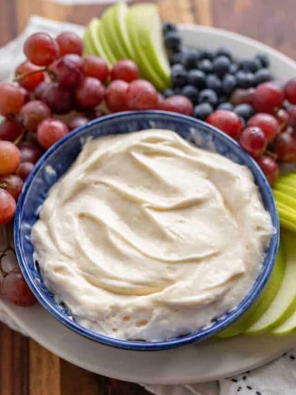 fruit dip in a bowl with grapes blueberries and green apples sliced around it
