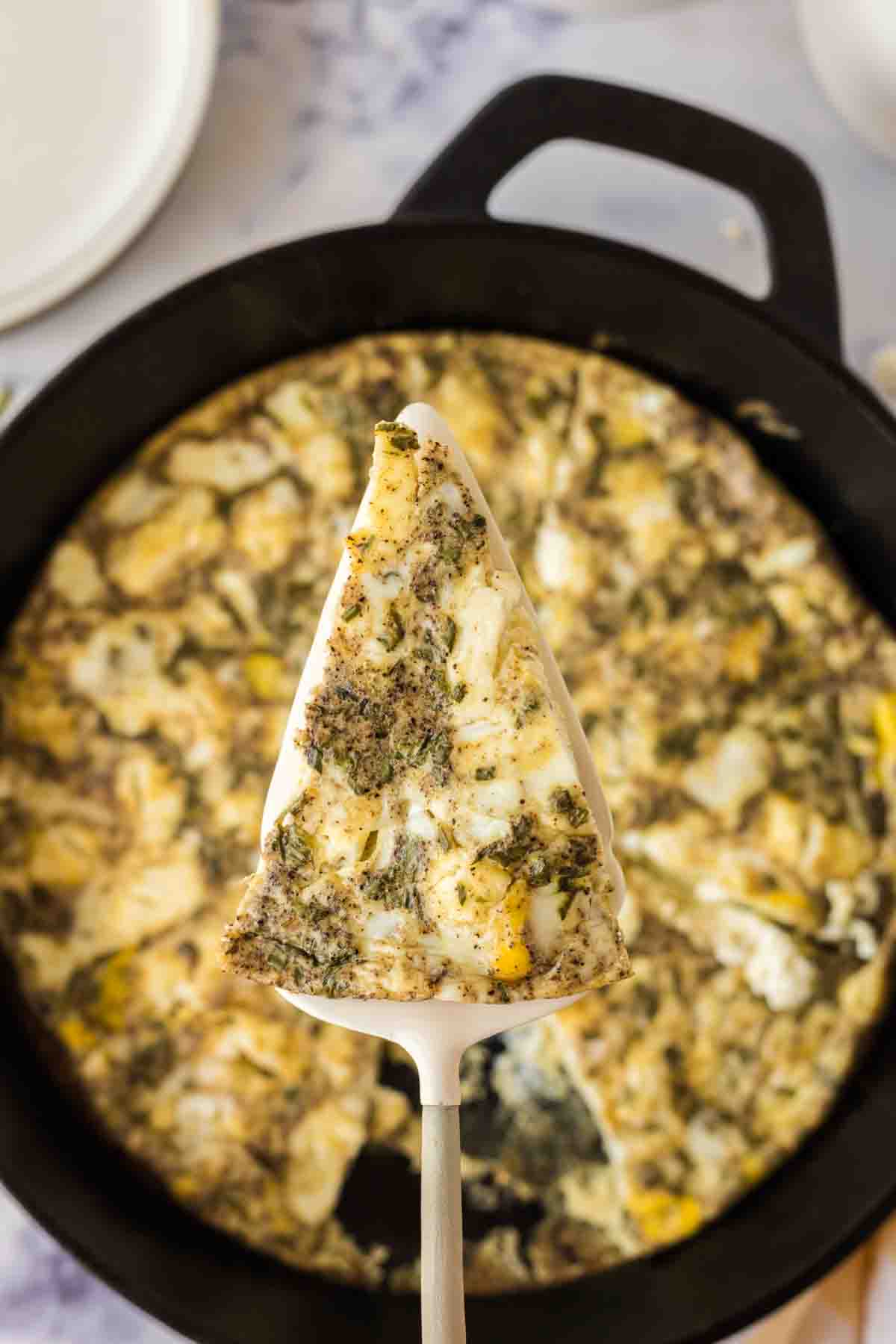 frittata baked in a cast iron pan and a slice on a spatula in the close up
