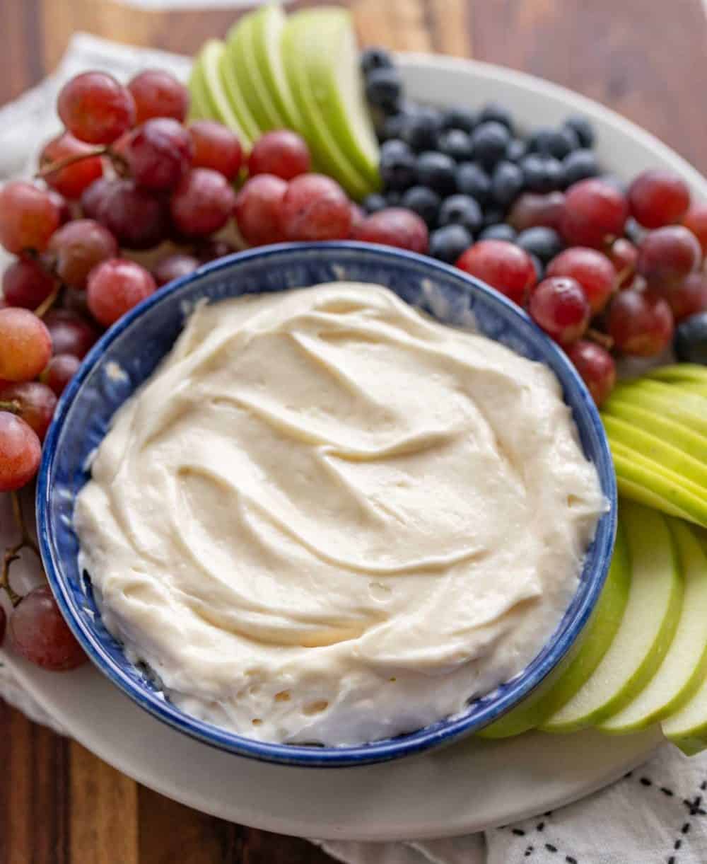 fruit dip in a bowl with grapes blueberries and green apples sliced around it