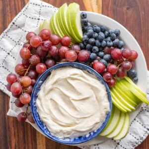top view of fruit dip in a bowl with grapes blueberries and green apples sliced around it