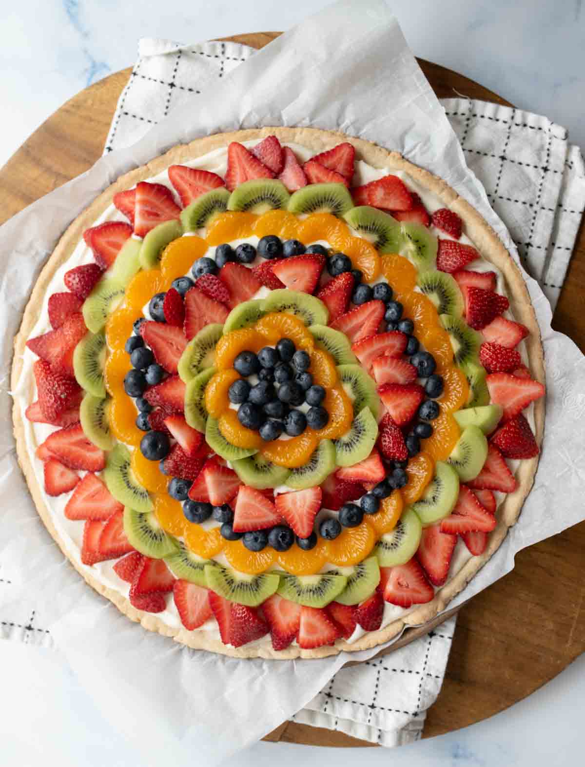 top view of a whole fruit pizza with slices of colorful fruit organized in a near mandala design on a round plate