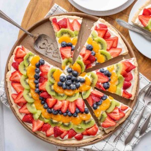 top view of a sliced fruit pizza with slices of colorful fruit organized in a near mandala design on a round plate