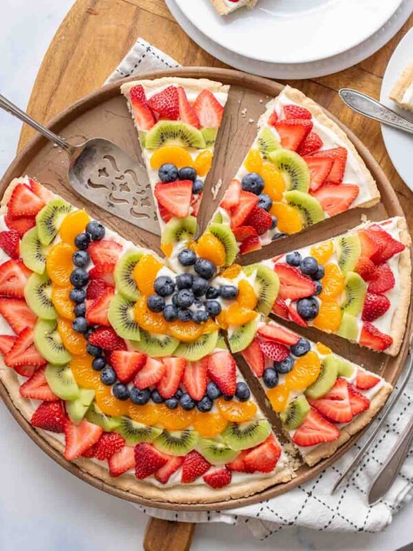 top view of a sliced fruit pizza with slices of colorful fruit organized in a near mandala design on a round plate