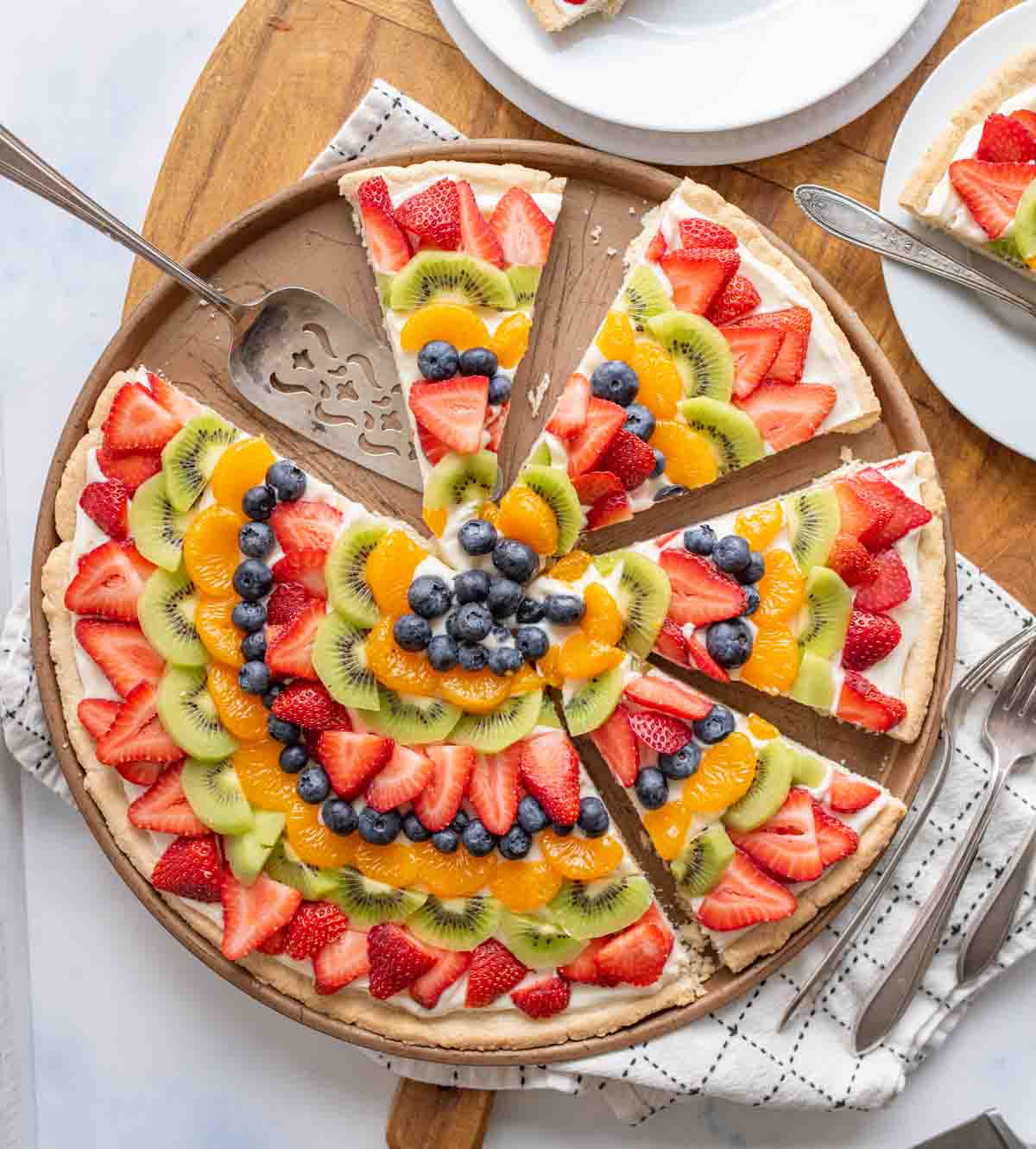 top view of a sliced fruit pizza with slices of colorful fruit organized in a near mandala design on a round plate