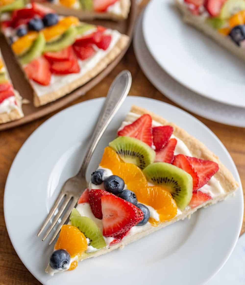one sliced served out of a fruit pizza with slices of colorful fruit organized in a near mandala design on a round plate