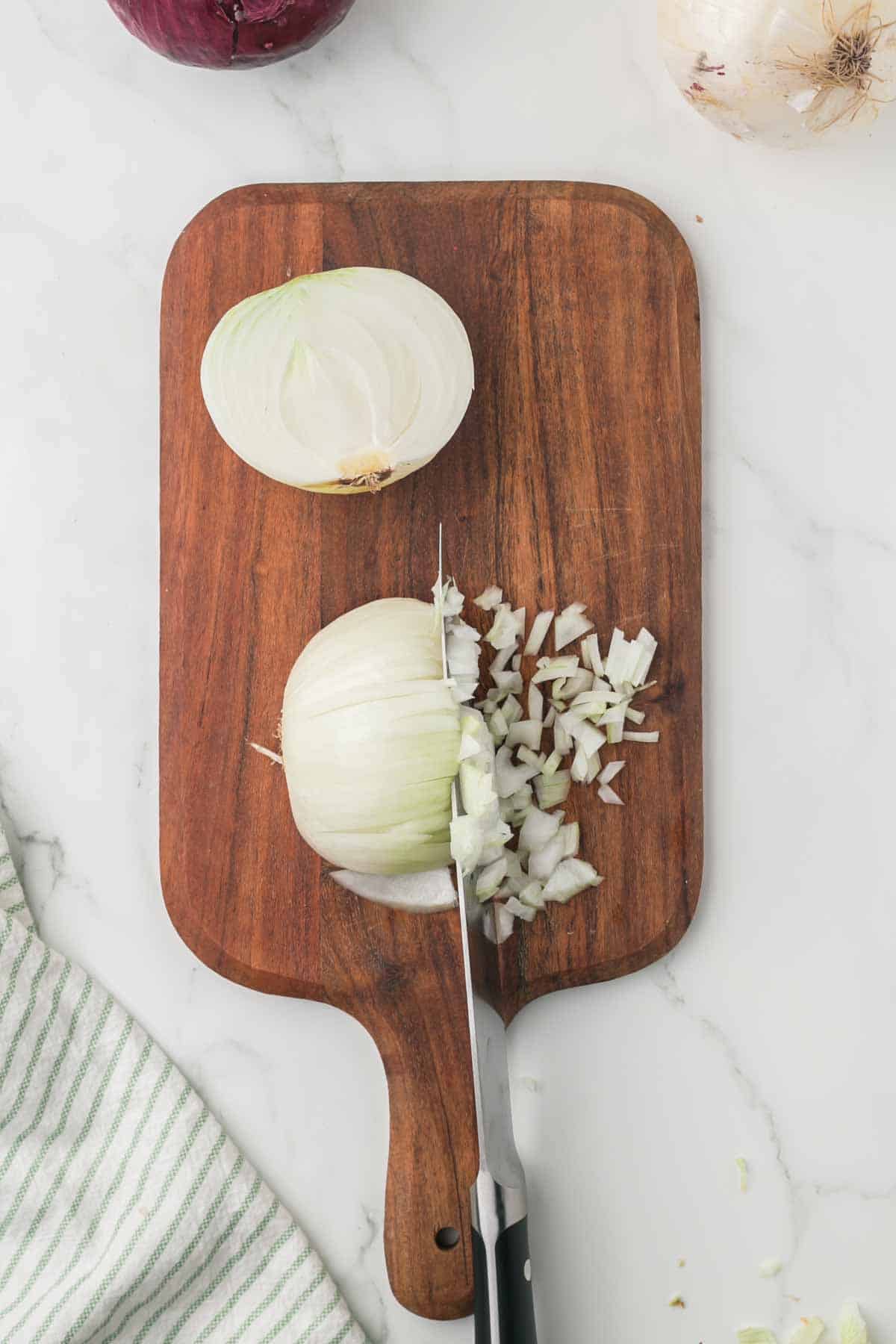 how to dice an onion, white onion on a wooden chopping block step by step