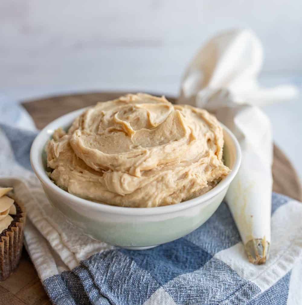 fluffy peanut butter frosting in a bowl with whipped beige peaks and piped onto a cupcake