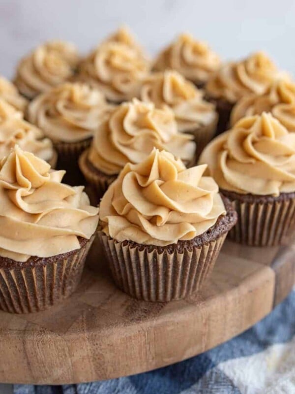 fluffy beige frosting pipped onto a plate of chocolate cupcakes