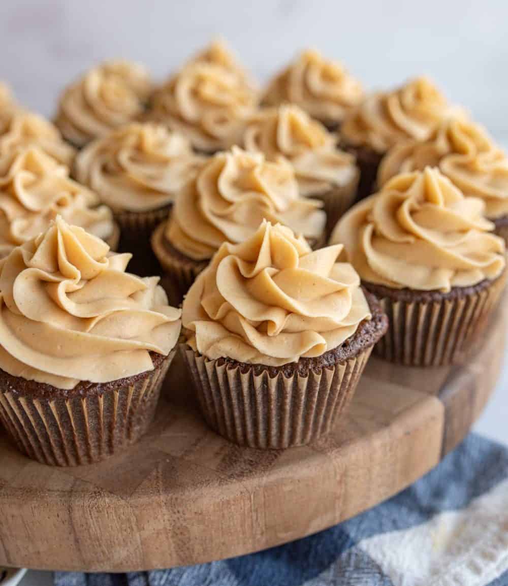 fluffy beige frosting pipped onto a plate of chocolate cupcakes