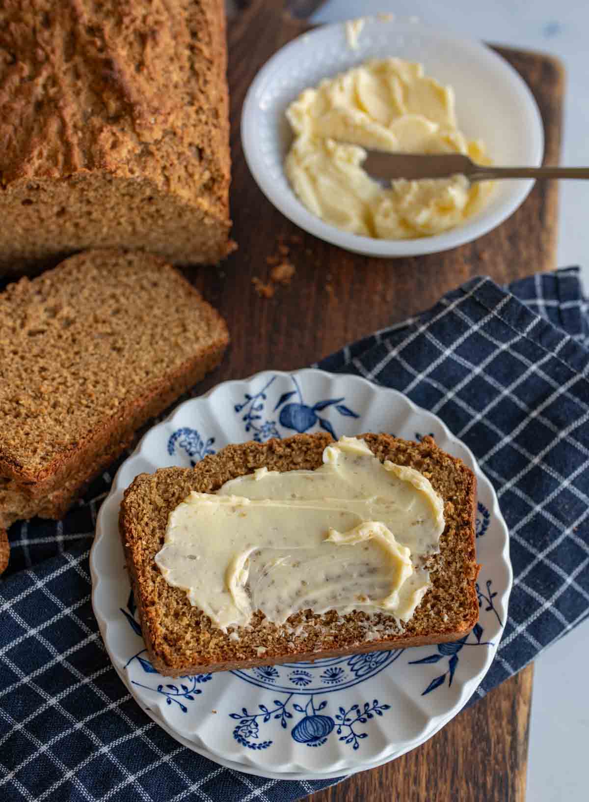 aesthetic view of a slice of soda bread and a spread of butter and a whole loaf and plate of butter in the background