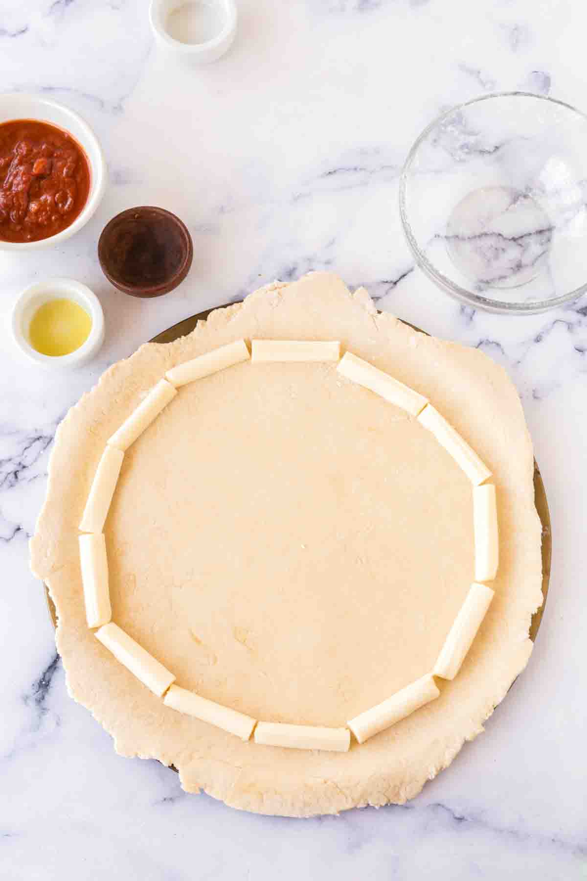 stuff crust pizza dough laid out and cheese sticks for the crust