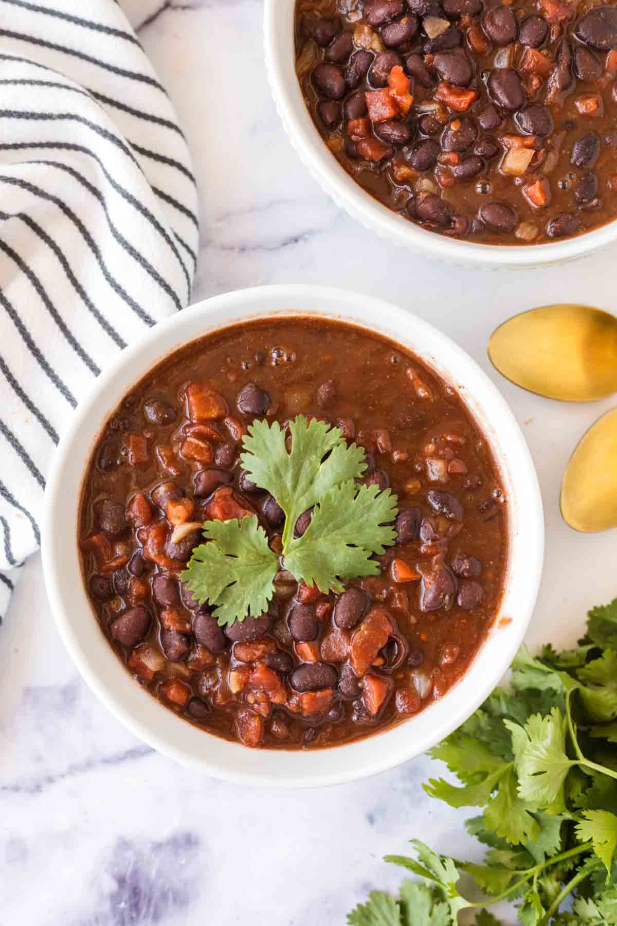 two white bowl with vegetarian chili and golden spoons with cilantro on top