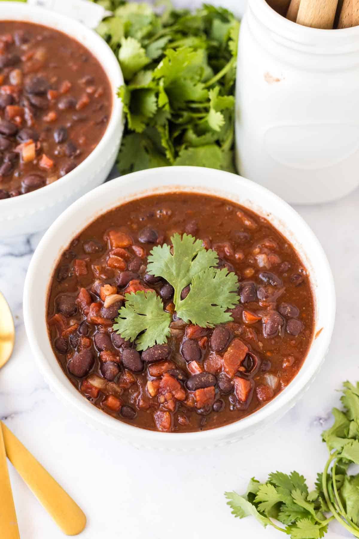 white bowl with vegetarian chili and golden spoons and cilantro on top