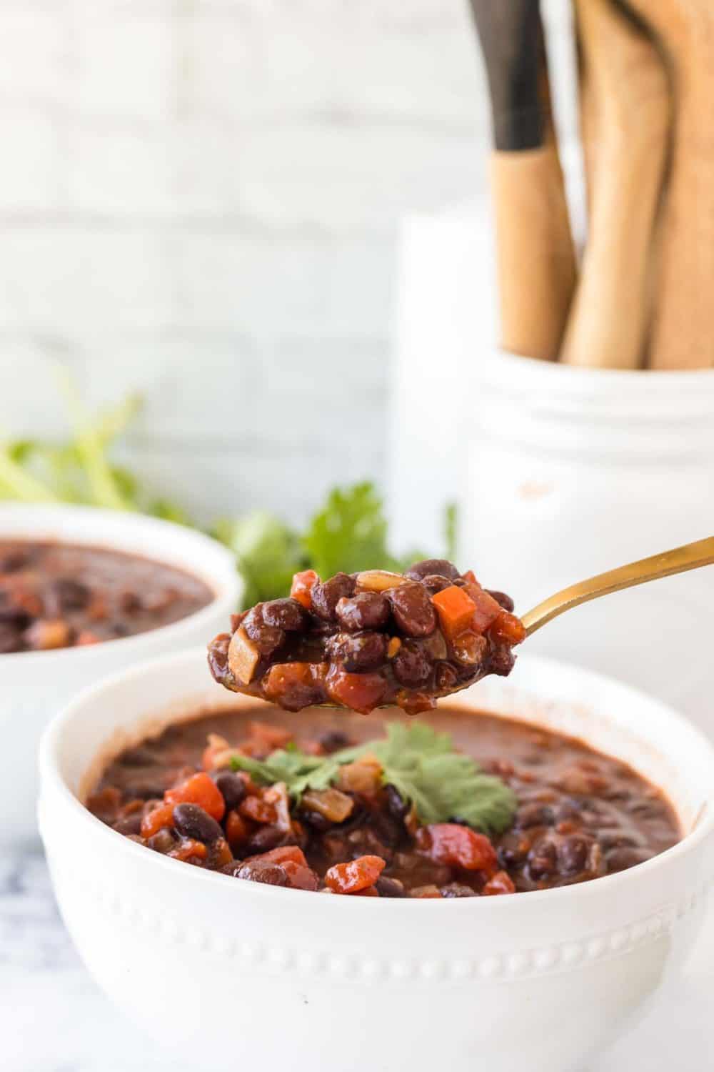 white bowl with vegetarian chili and golden spoons and cilantro on top