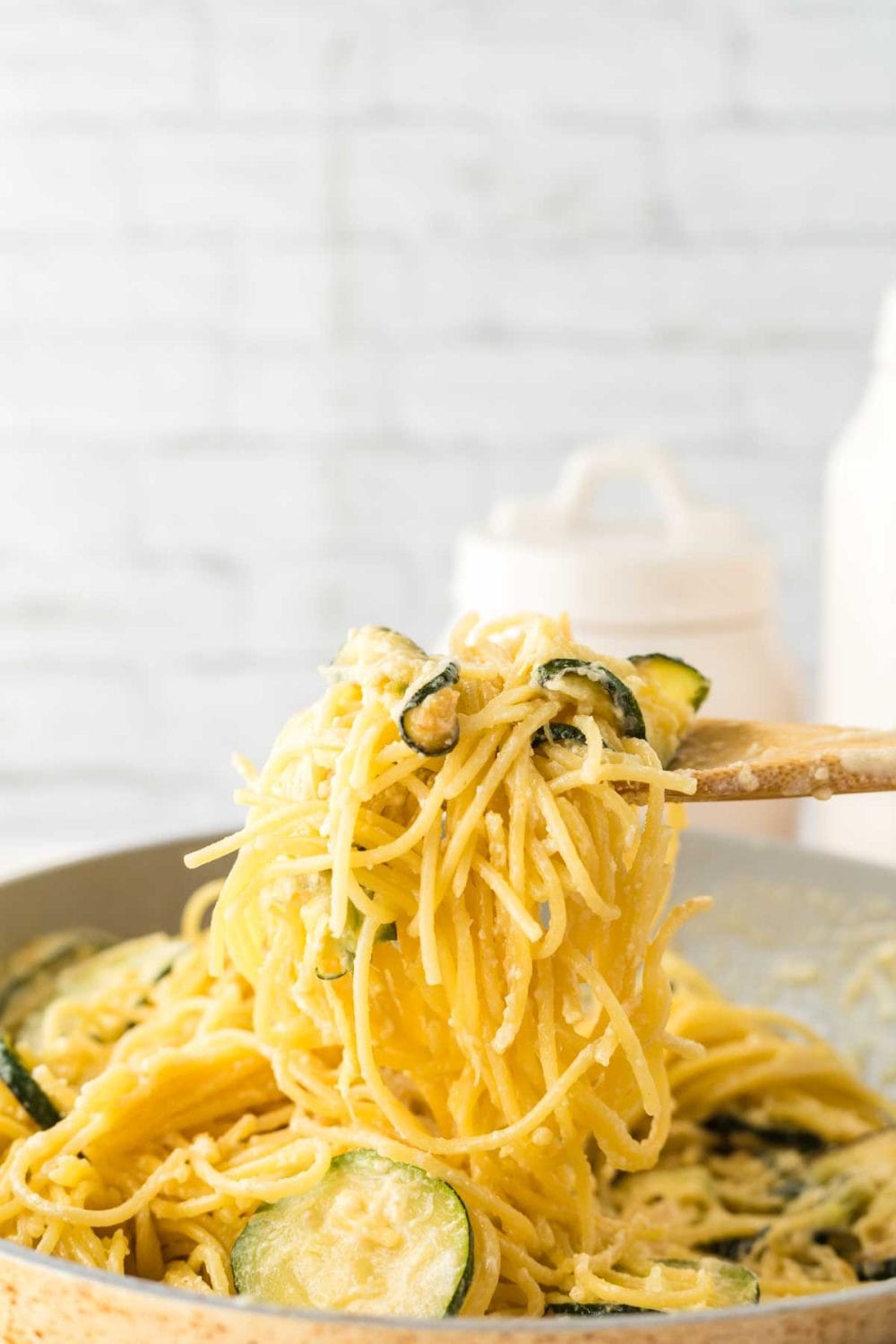 sliced zucchini in a pan with pasta and a wooden spoon