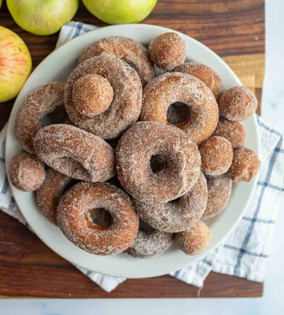 top view of apple cider donuts and holes dusted with sugar on a white plate.
