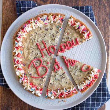 large round chocolate chip cookie cake with birthday decorations sliced