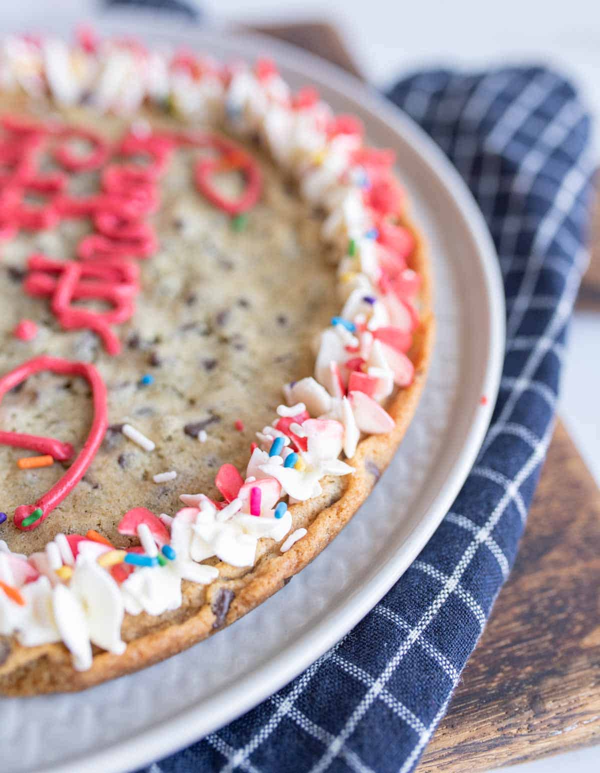 close up of the edge of alarge round chocolate chip cookie cake with birthday decorations