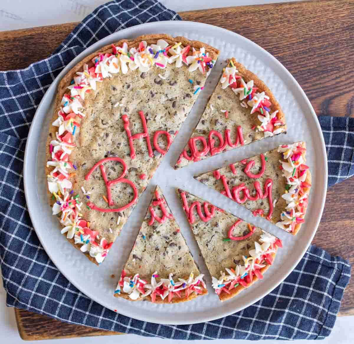 top view of a alarge round chocolate chip cookie cake with birthday decorations sliced