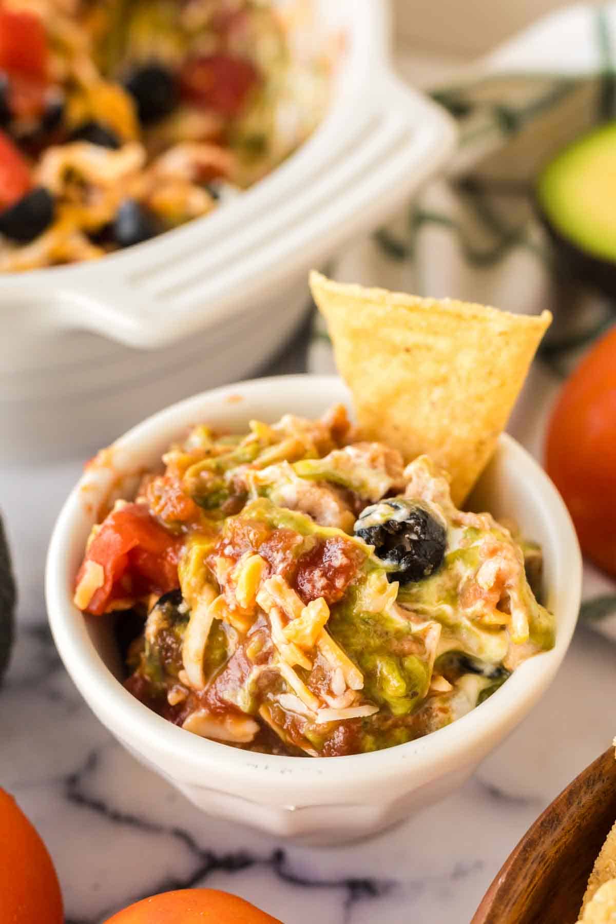 7 layer dip recipe in a small dish with a chip