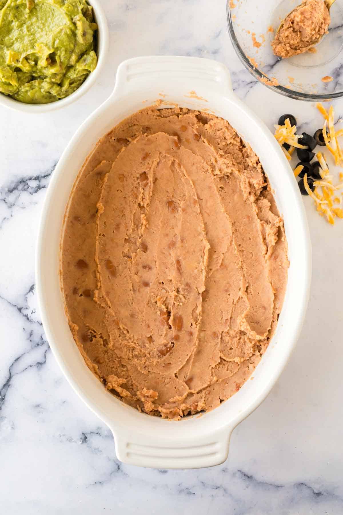 white baking casserole dish with 7 layer dip being made