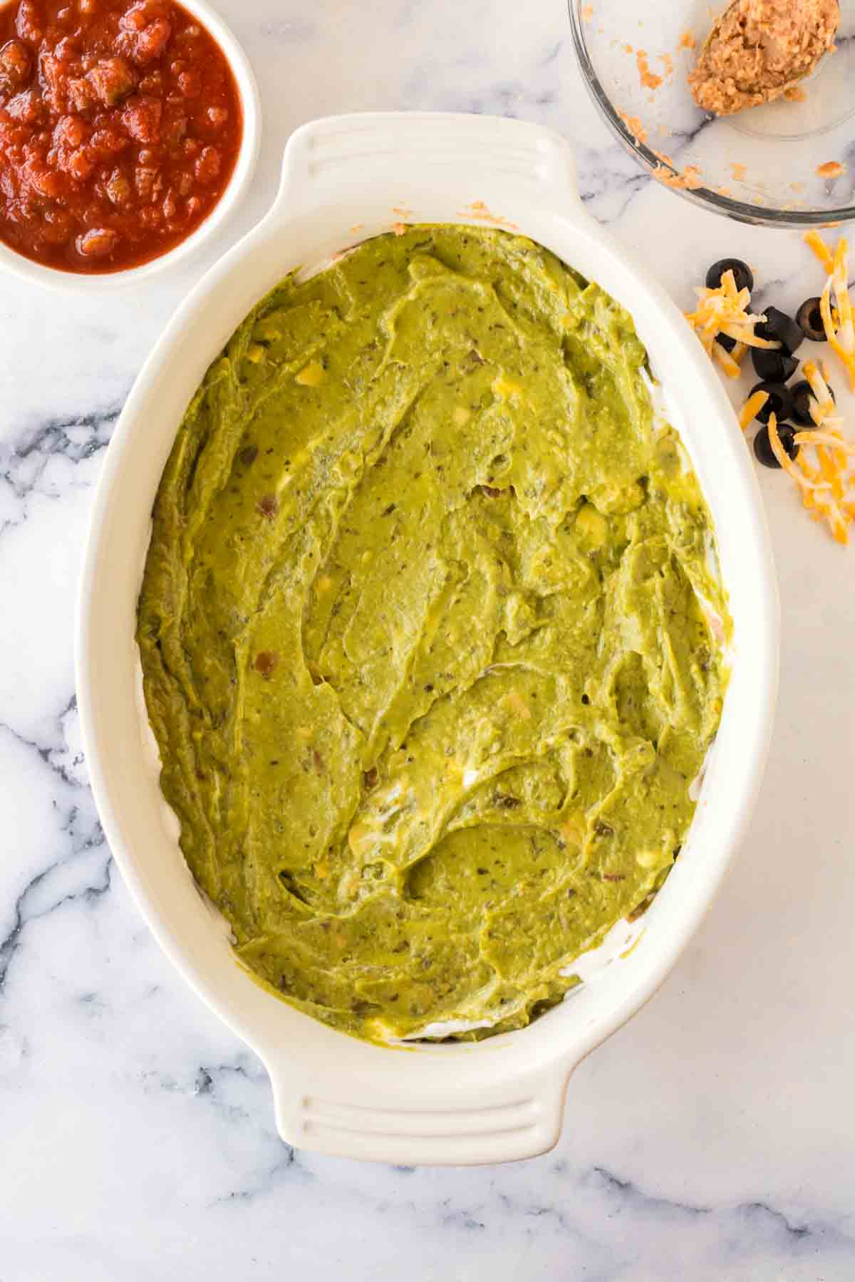 white baking casserole dish with 7 layer dip being made