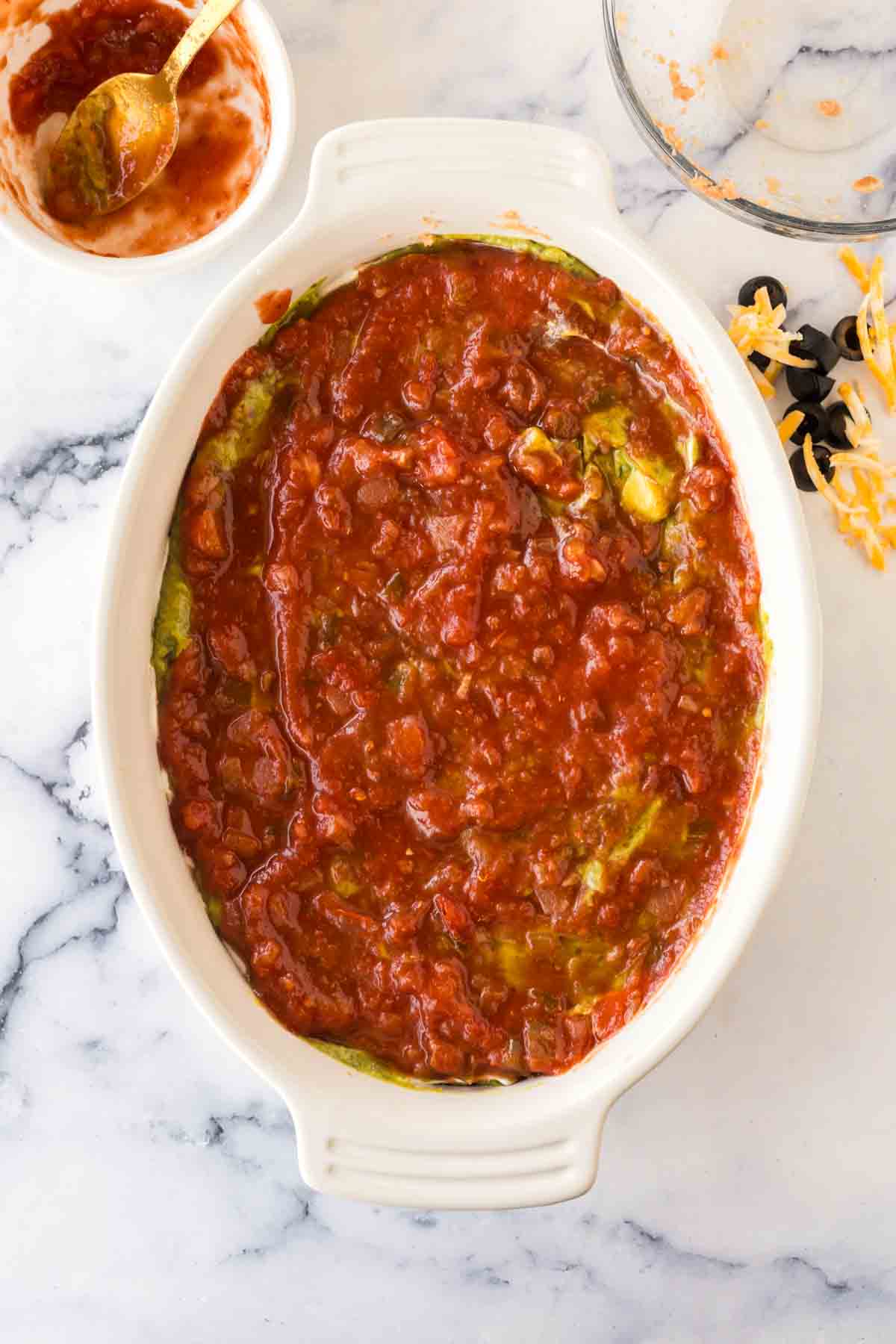 white baking casserole dish with 7 layer dip being made