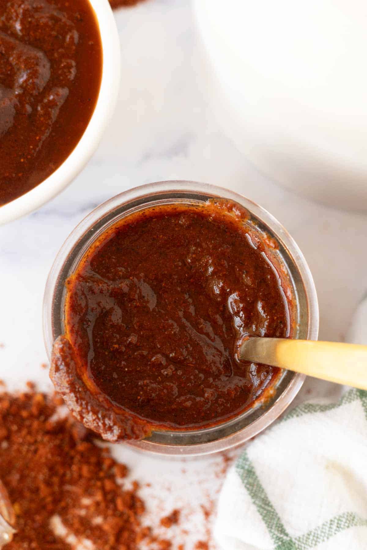 Spoon inside of a jar of red adobo sauce.