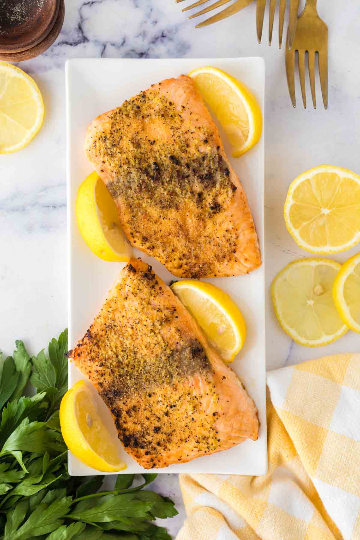 Cooked salmon filets served on a white plate with lemons.