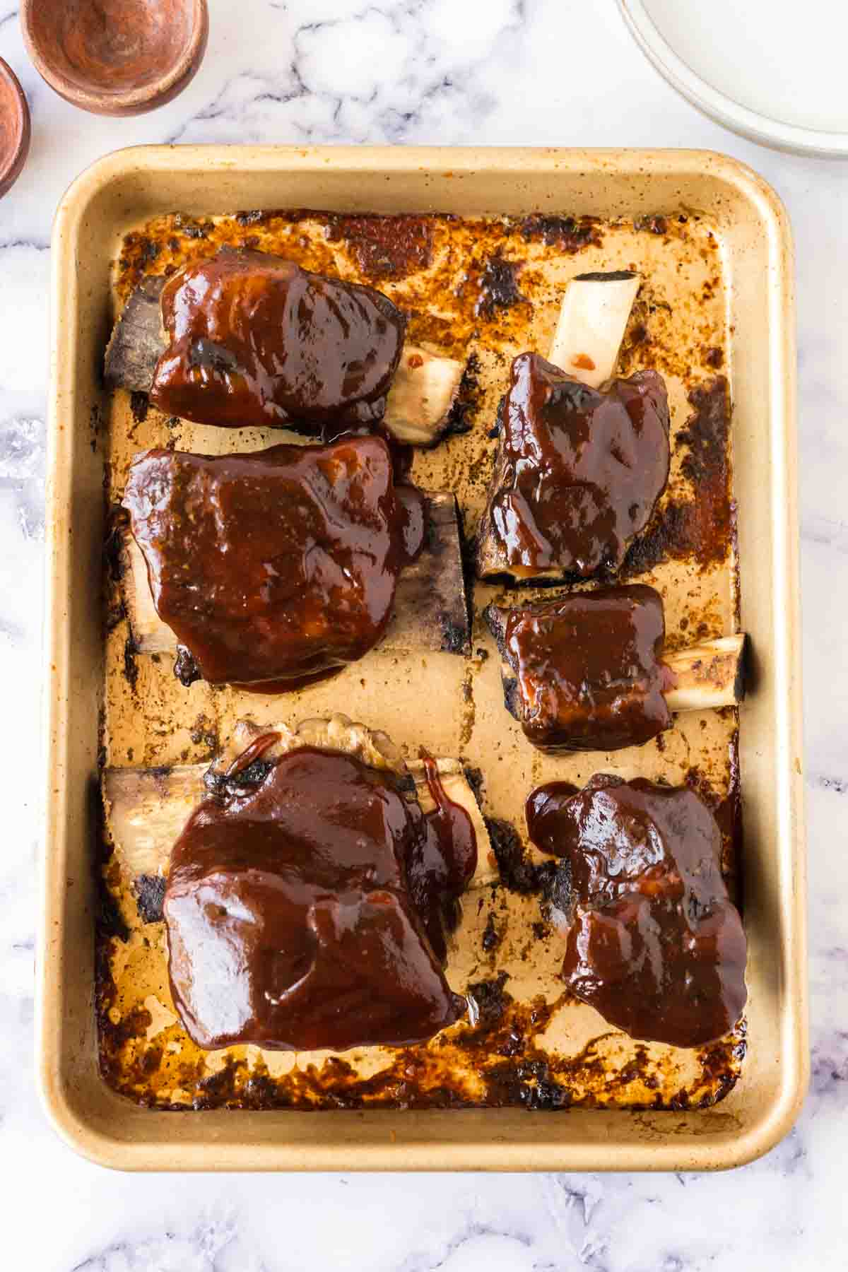 Beef short ribs covered in bbq sauce on a baking sheet.